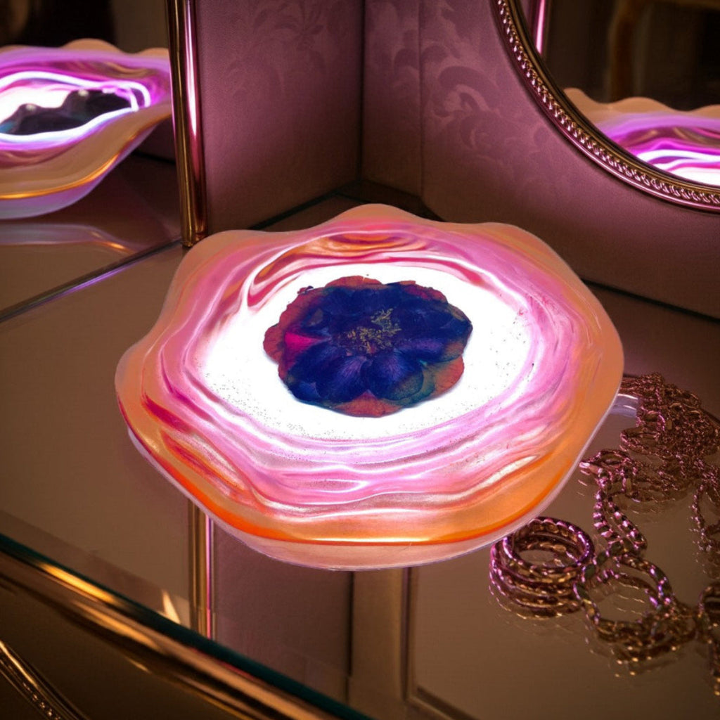 Decorative Trays - A glowing resin jewellery decorative tray with wavy pink, orange, and white edges, a purple floral centre and a mirrored surface reflecting its light.