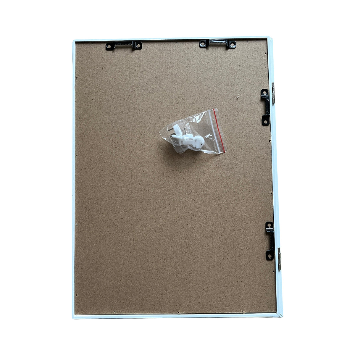 Back of a shadowbox with white fixings in a clear bag on a brown cardboard surface with metal brackets.
