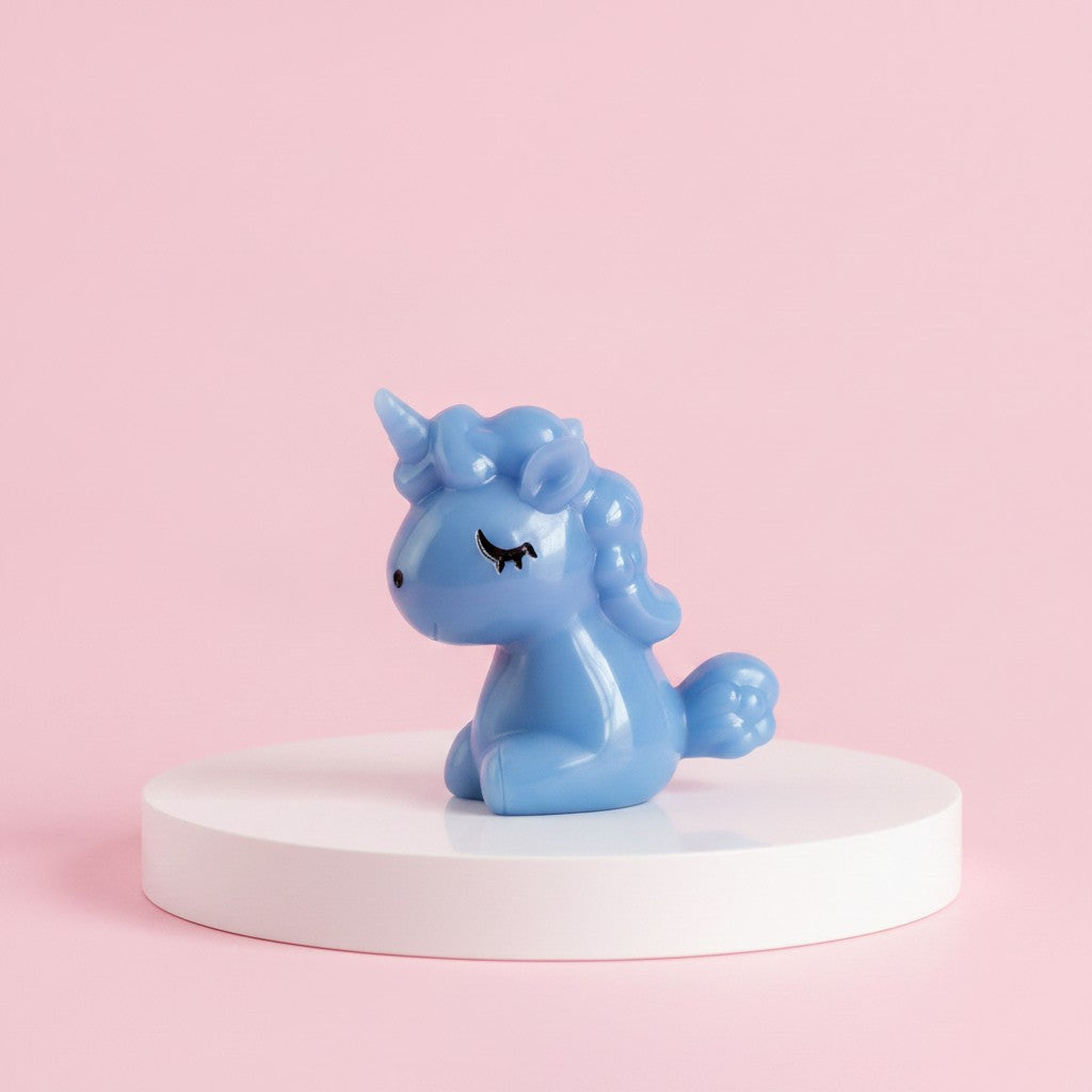 A small glossy blue unicorn figurine with closed eyes sits centered on a round white pedestal against a soft pink background.