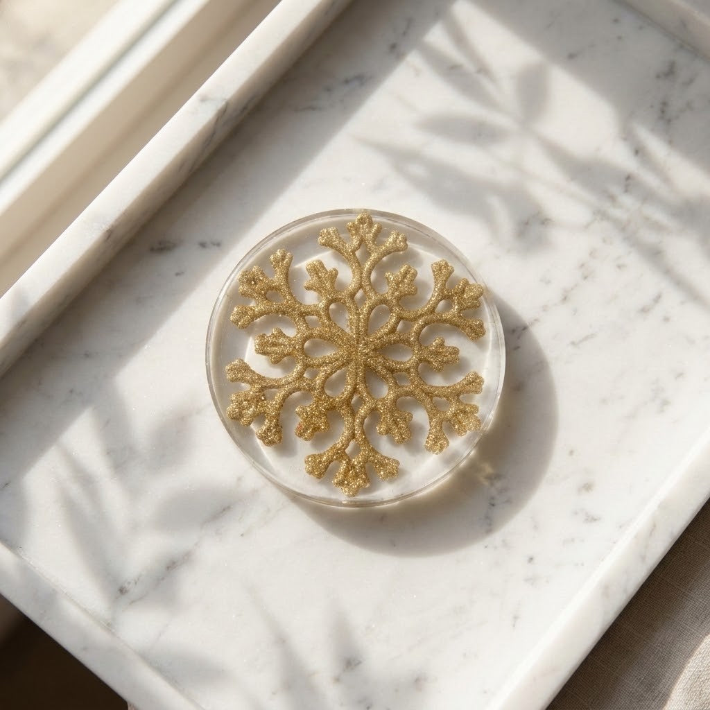 Christmas Snowflake Coaster - A round clear resin coaster featuring a glittery gold snowflake design, resting on a white marble tray with soft leaf shadows.