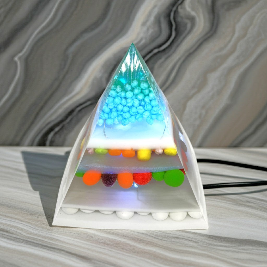 Triangular Pyramid LED lamp filled with colourful sweets, on a grey marble counter top.