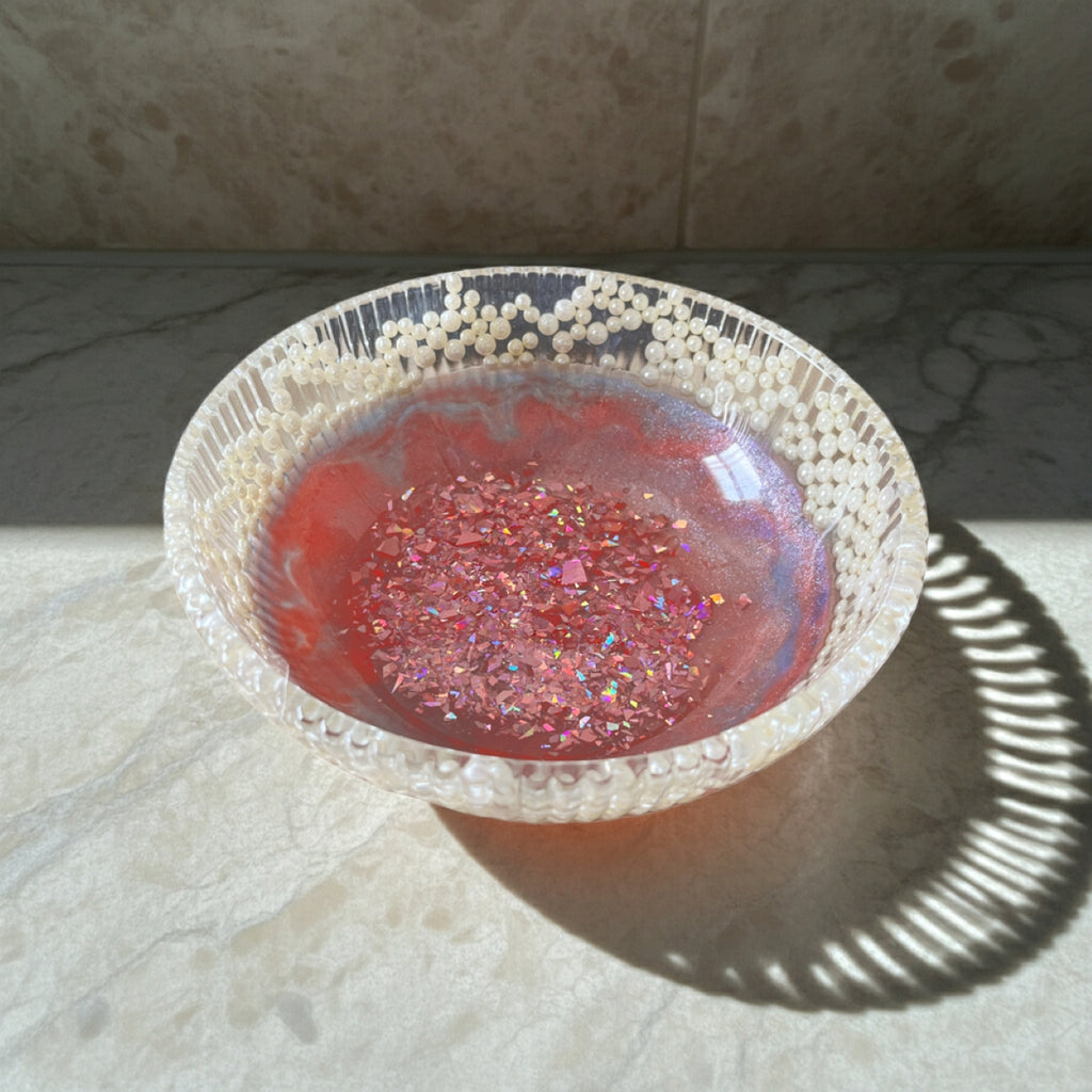 Decorative pink glitter bowl with white pearl beads around the rim, on a marble surface