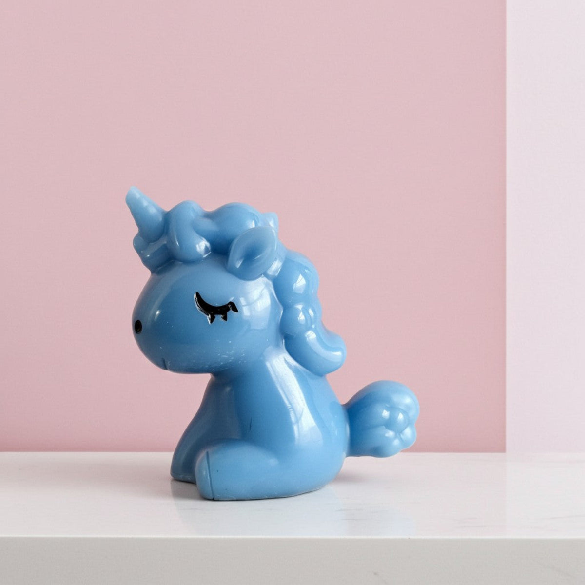 Blue unicorn figurine on a white surface with a pink background