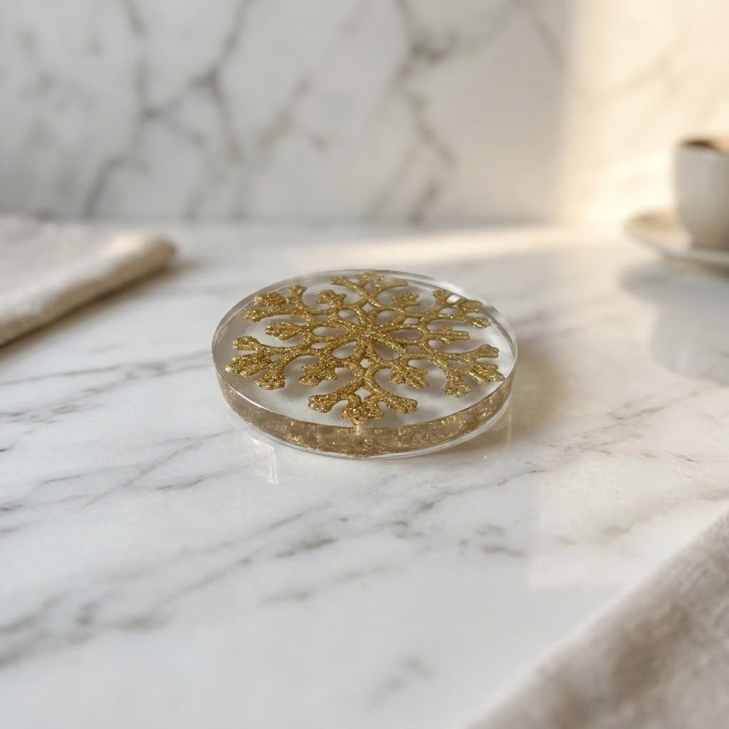 Christmas Snowflake Coaster - A round clear resin coaster with a glittery gold snowflake design, resting on a white marble surface.
