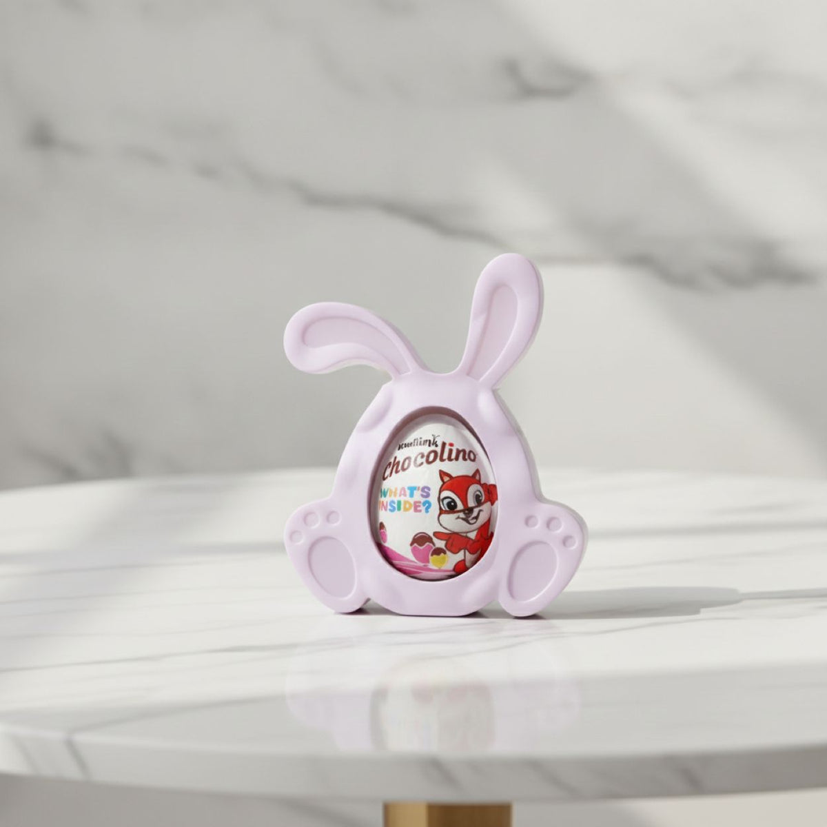 A light purple bunny-shaped chocolate holder displaying a Chocolino chocolate egg, set on a white marble table with a matching marble background.
