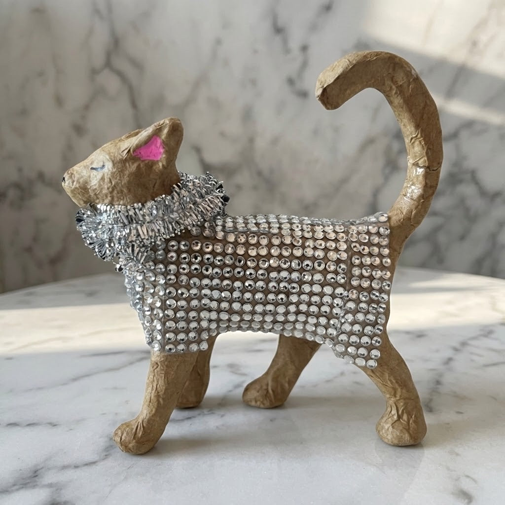 Diamante Cat Figurine -  Side view of a decorative cat figurine with a textured tan body covered in silver rhinestones, wearing a matching silver rhinestone collar, set on a white marble surface with a marble-patterned background.