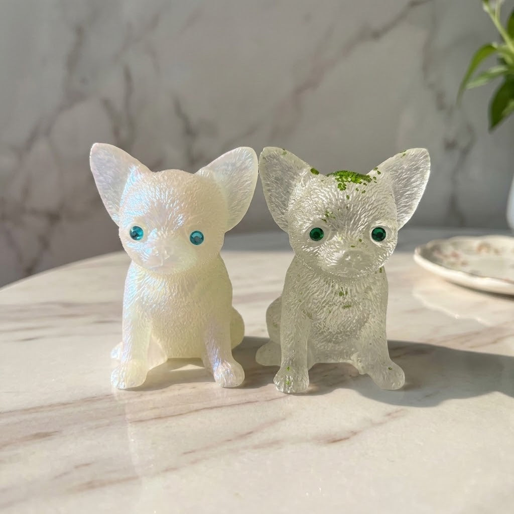 Chihuahua Dog Figurines - Two small dog figurines on a light marble surface. One is opaque milky white with blue eyes, and the other is translucent clear with tiny green flecks and green eyes.