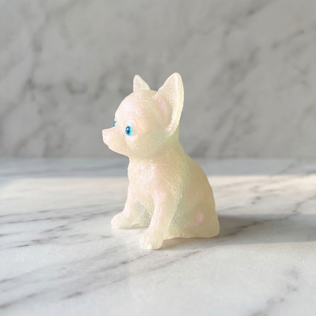 Chihuahua Dog Figurines - Side view of a small translucent figurine of a seated puppy or dog with bright blue eyes, placed on a white marble surface against a softly blurred marble background.
