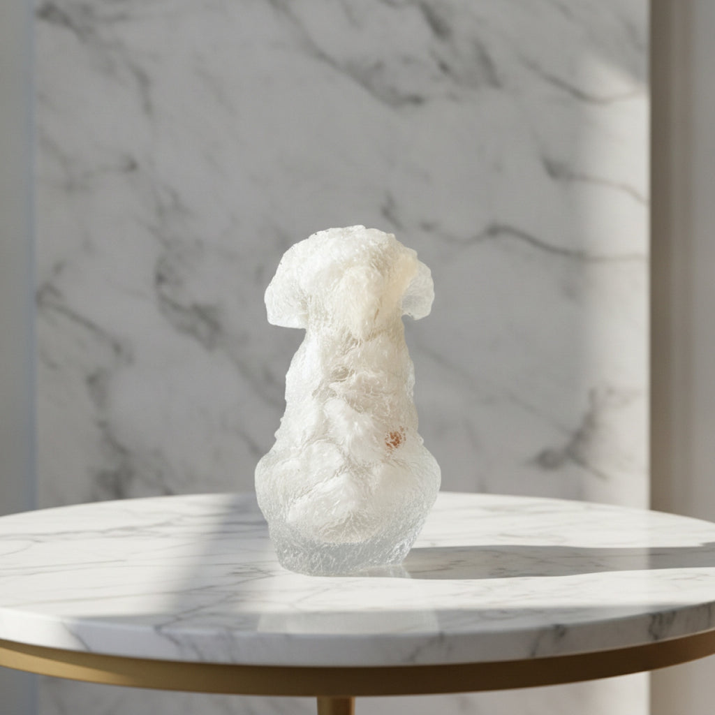 A small white textured decorative object resembling a stylized back of a dog displayed on a round white marble table with a gold-toned edge against a marble-patterned wall. 