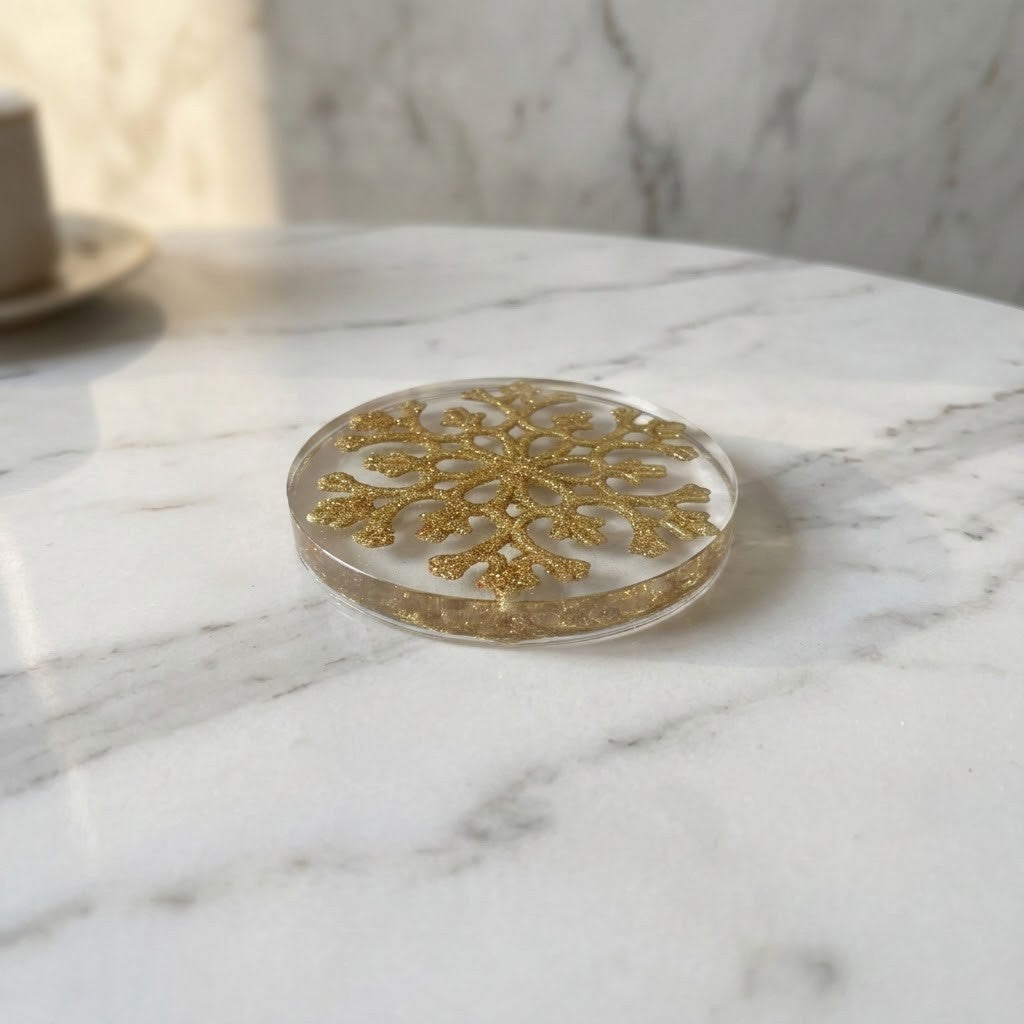 Christmas Snowflake Coaster - A round clear resin coaster with a glittery gold snowflake design, resting on a white marble surface.