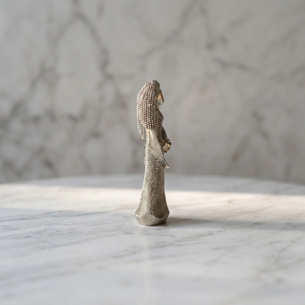 Christmas Angel Figurine - A small metallic figurine of a robed angel or saint, shown from the side, standing on a white marble surface with a matching marble background.