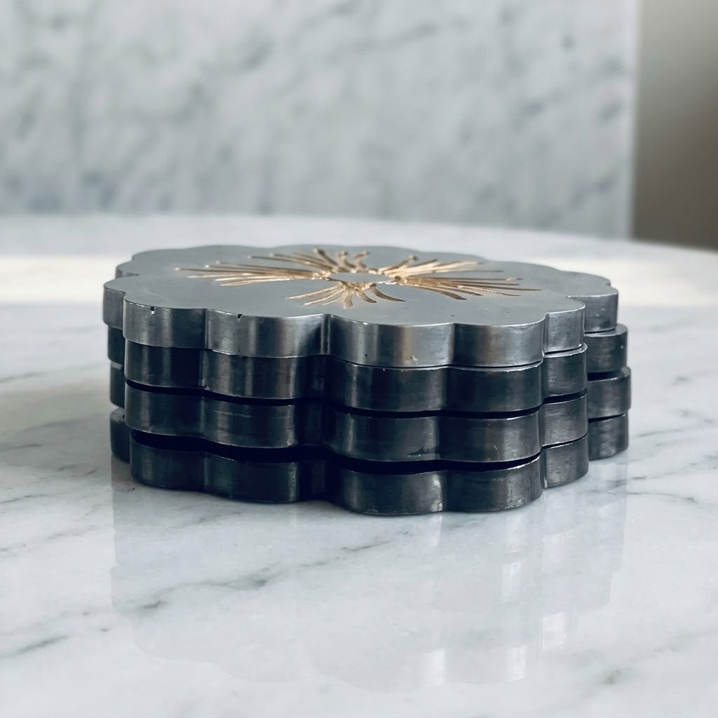 Scalloped Floral Coasters - A stack of dark grey scalloped coasters with a metallic gold sunburst design in the centre, displayed on a white marble surface.