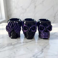 Resin Skull Pots - Set of 3 black and purple skull containers, with skeleton hands on a grey marble surface and background.