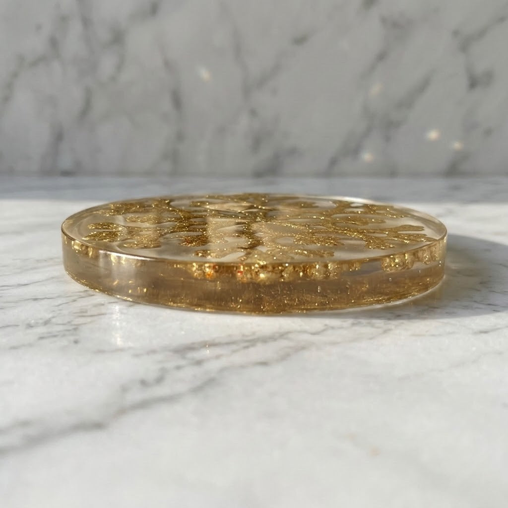 Christmas Snowflake Coaster - A round, clear resin coaster or trivet filled with shimmering gold glitter, resting on a white marble surface with a matching marble background.