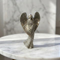 Christmas Angel Figurine - A textured silver angel figurine with outstretched wings, standing on a white marble surface with a blurred marble background.