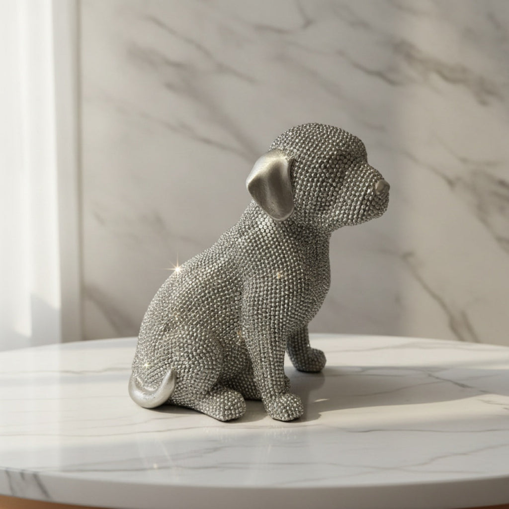 A silver dog figurine covered in small silver rhinestones, side view sitting on a white marble surface against a marble-patterned wall.