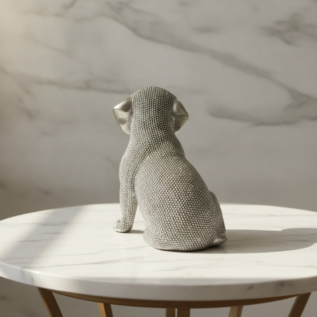 A textured silver dog figurine, back view sitting on a white marble-topped side table against a marble-patterned wall.