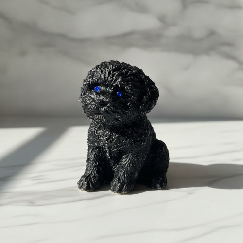 A small black textured figurine of a curly-haired puppy with bright blue eyes, sitting on a white marble surface with a matching marble background.