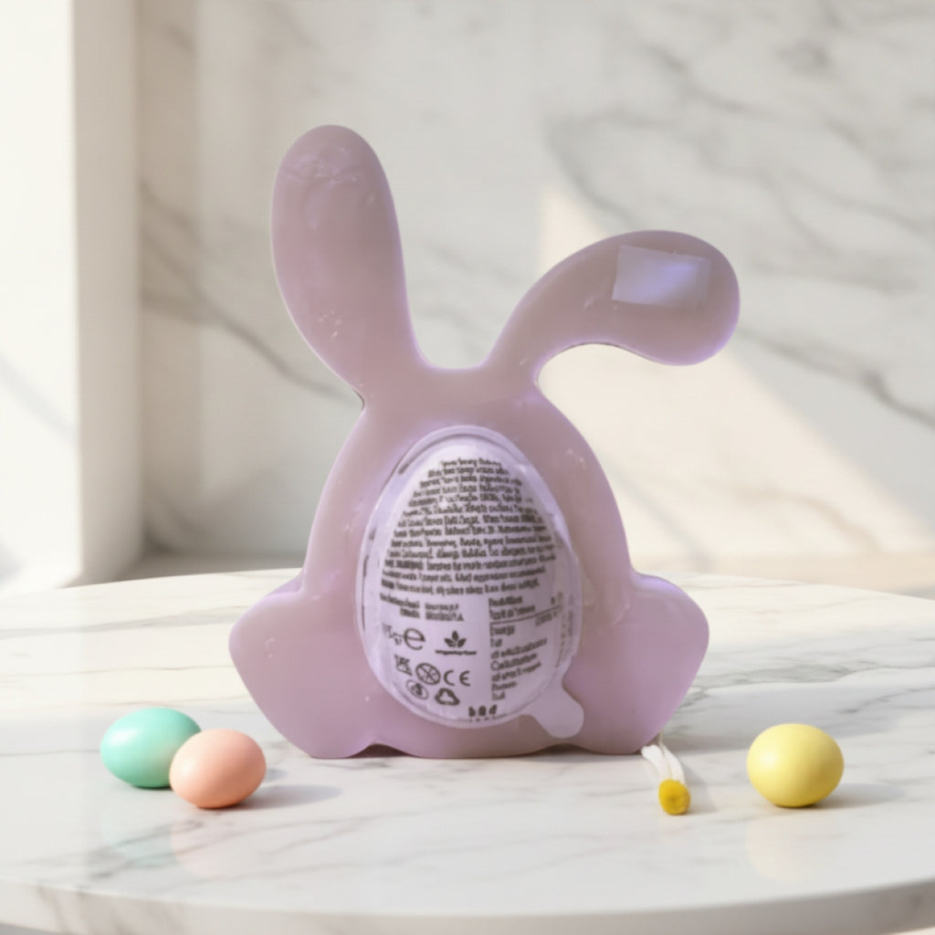 A lavender purple bunny-shaped egg holder with an egg product label on the back, displayed on a white marble surface with pastel eggs nearby.