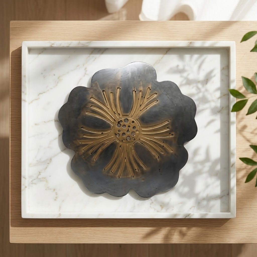 Scalloped Floral Coasters - A scalloped grey and gold coaster with a sunburst centre, shown on a white marble tray with and leaves in the background.