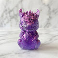 Baby Dragon Figurines - A small purple glittery dragon figurine sitting on a white marble surface with a blurred white marble background.
