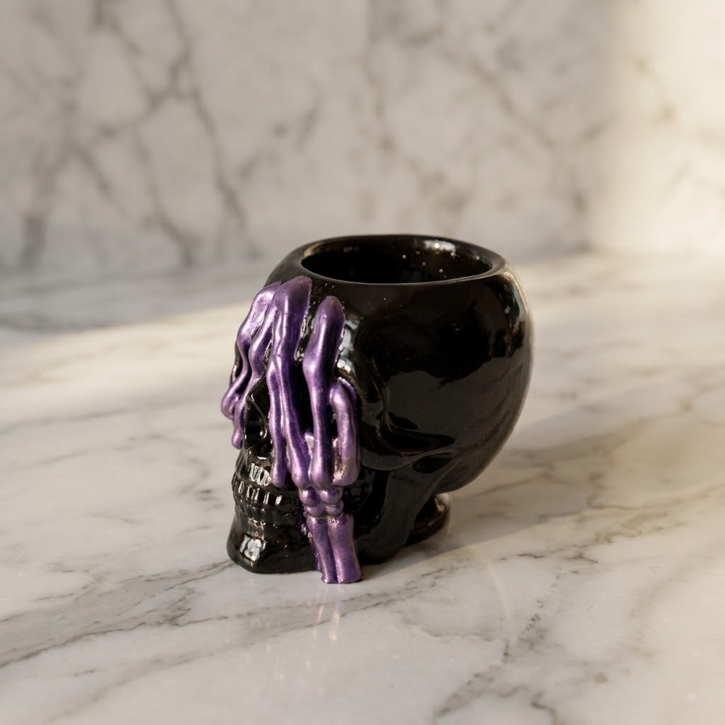 Resin Skull Pots - A glossy black skull-shaped cup with dripping purple paint details, set on a white marble surface against a matching marble background.