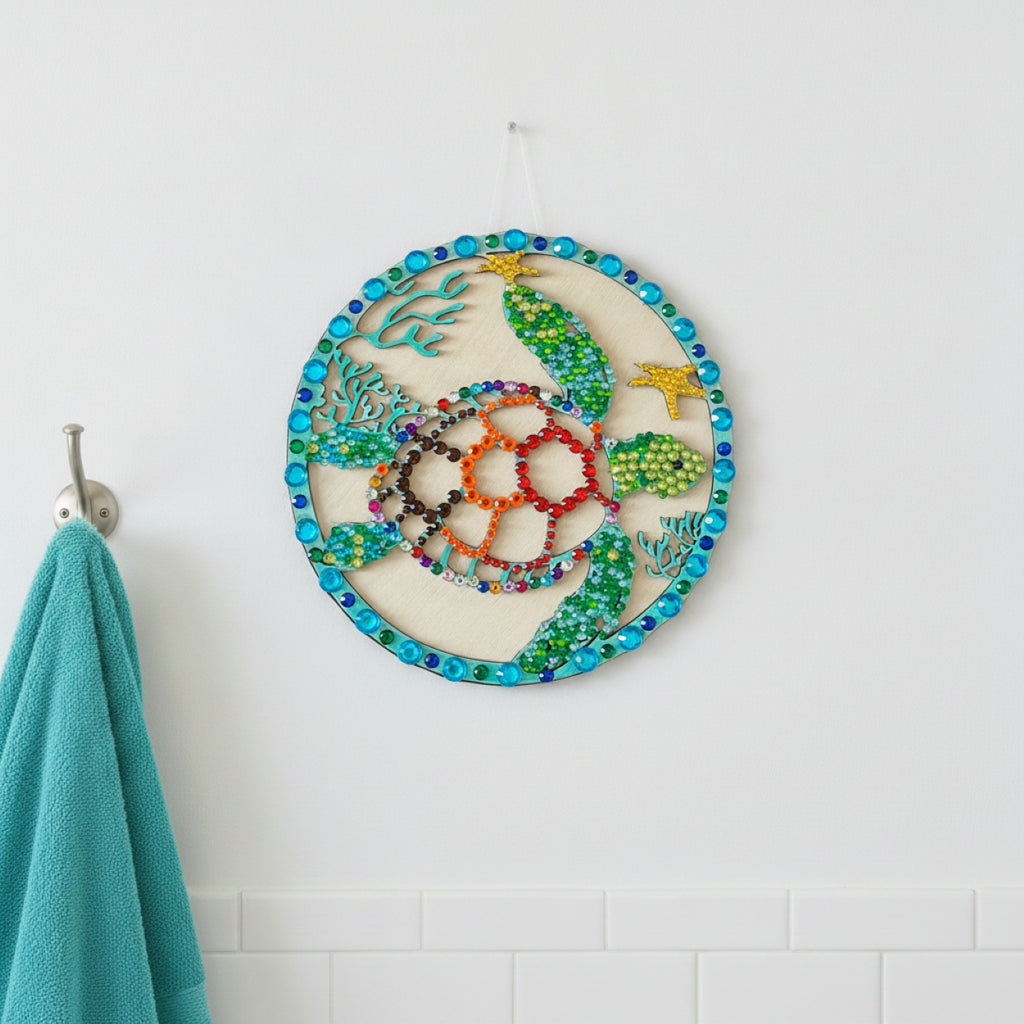 A circular beaded wall hanging featuring a sea turtle design with colorful beads, displayed on a white wall next to a teal towel on a hook.