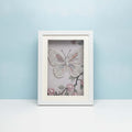 Framed artwork of a butterfly with pearls on a light blue background