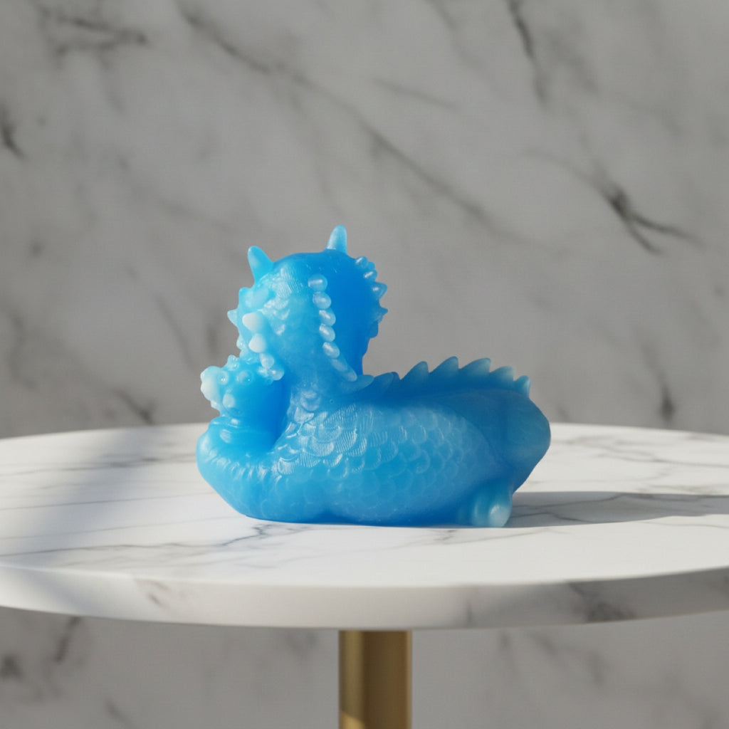 Back view of a small translucent blue dragon figurine sits on a round white marble table with a gold-colored leg, set against a matching marble background.